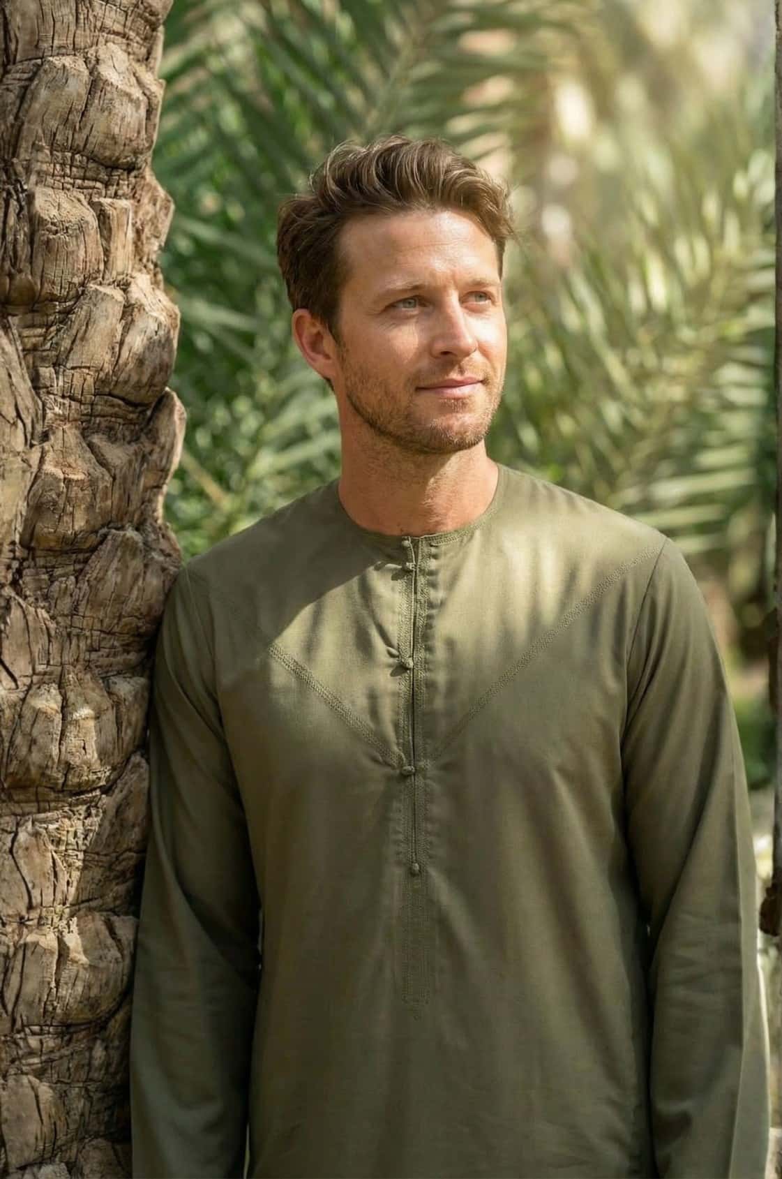 Adventurous Western man wearing an olive green kandora during a desert safari in Abu Dhabi, blending into the natural landscape. 2